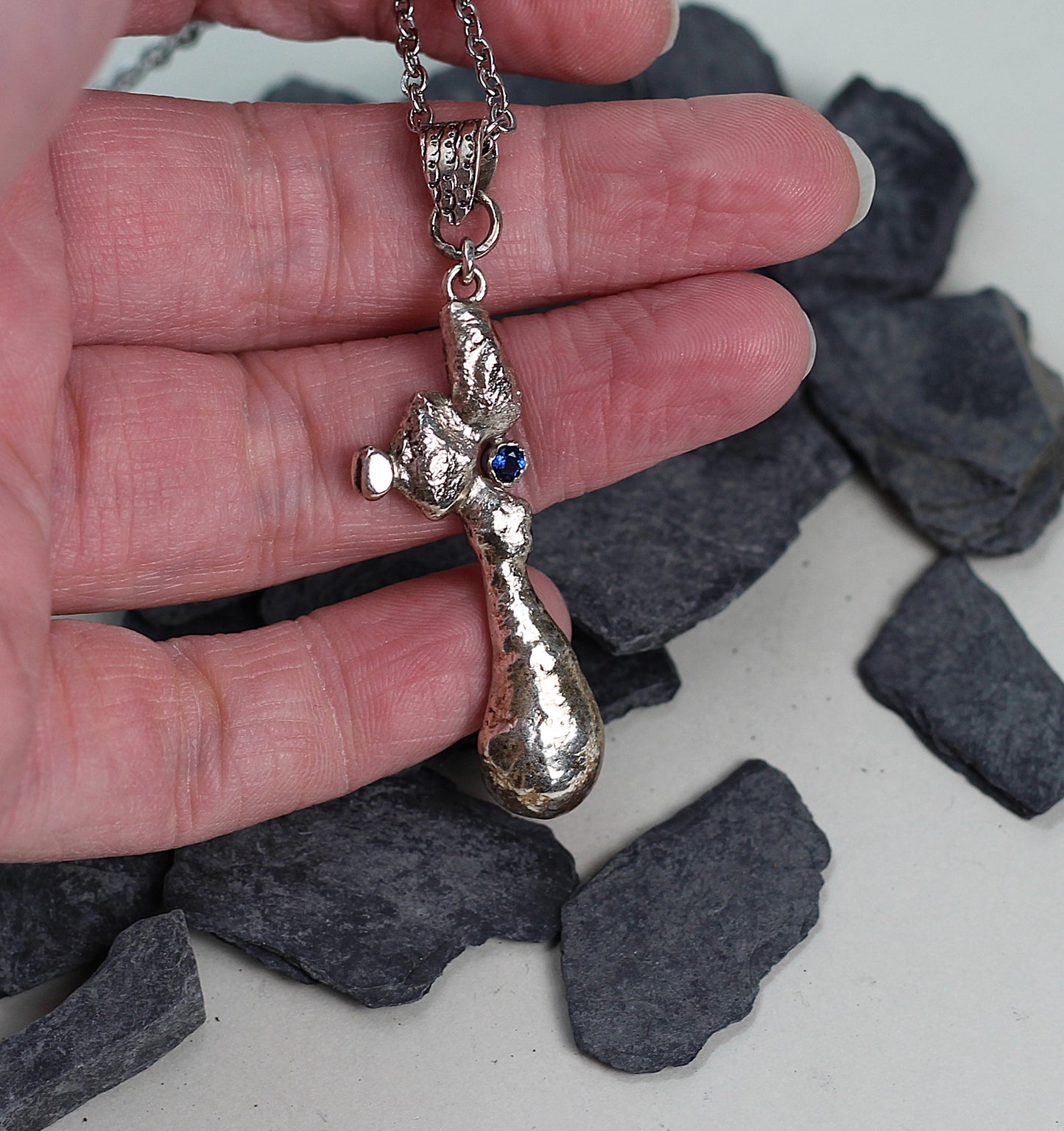 Unique handcrafted silver talisman with a volcanic molten finish and a tiny sapphire gem, showcasing authentic Austrian jewelry craftsmanship.