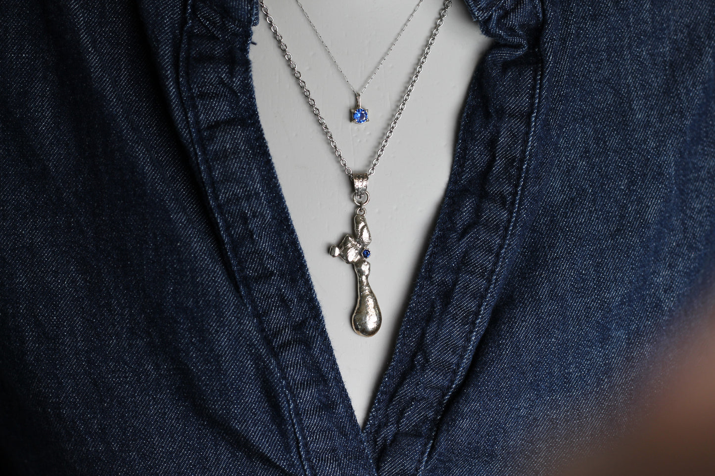 One-of-a-kind slow jewelry masterpiece featuring a heavy molten silver texture and a sparkling 2mm blue sapphire stone reflecting the natural light.