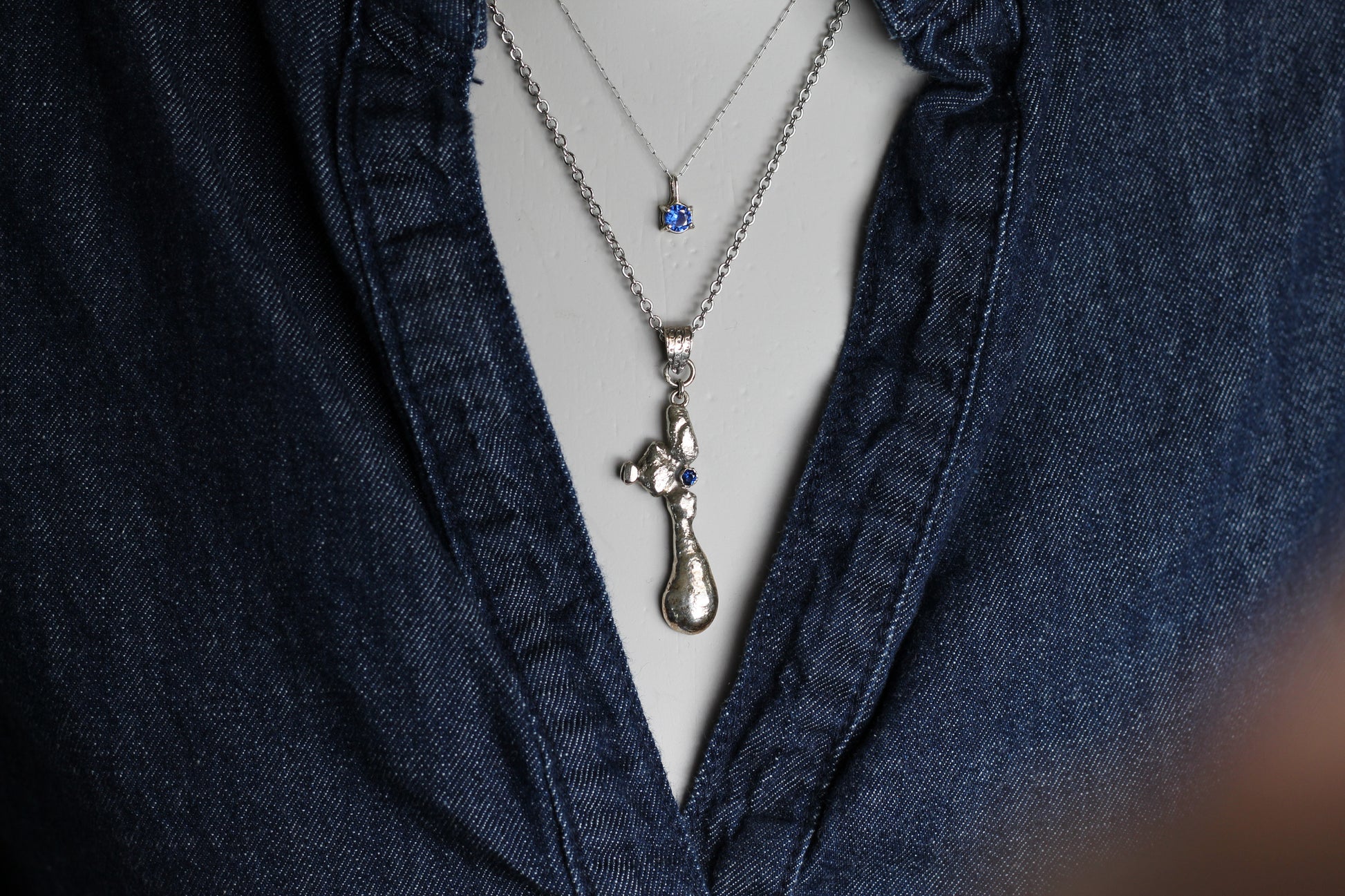 One-of-a-kind slow jewelry masterpiece featuring a heavy molten silver texture and a sparkling 2mm blue sapphire stone reflecting the natural light.