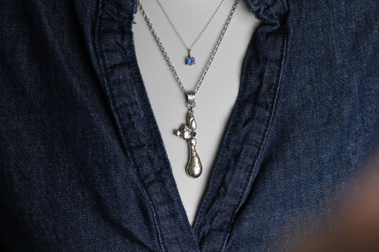 One-of-a-kind slow jewelry masterpiece featuring a heavy molten silver texture and a sparkling 2mm blue sapphire stone reflecting the natural light.