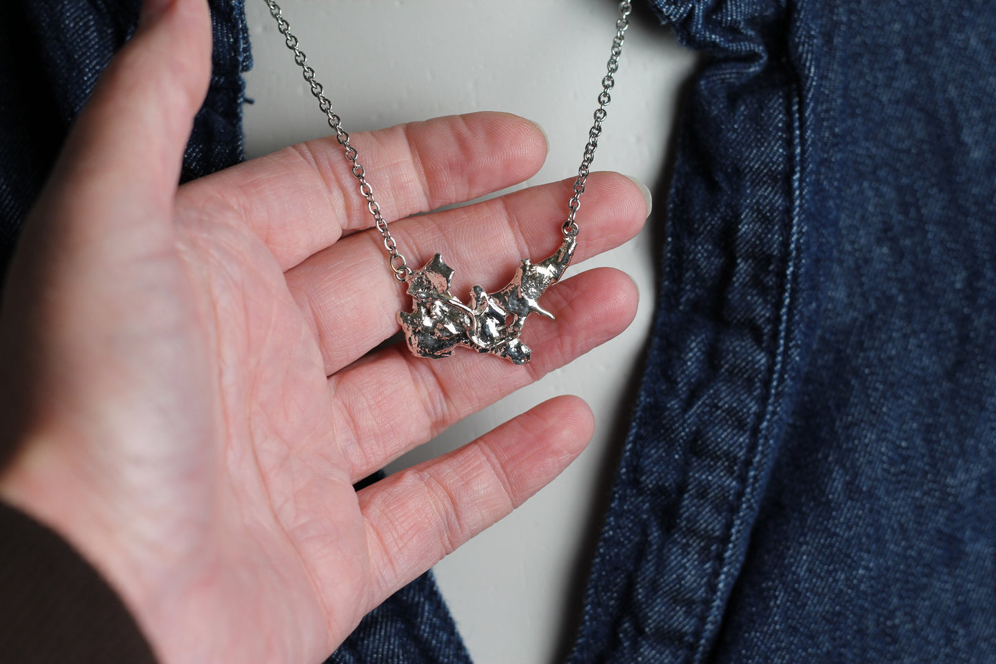 Detailed shot of an artisan statement necklace made of heavy melted 925 sterling silver , highlighting the unique raw edges.