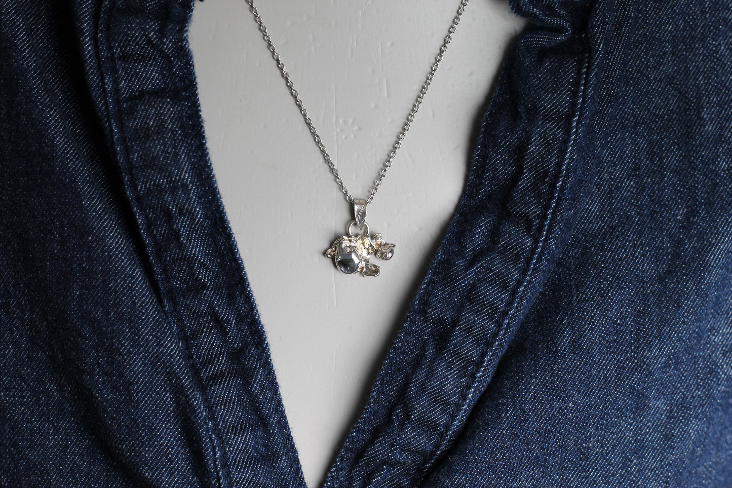 A woman wearing a minimalist molten silver necklace with a small sapphire stone, perfect for everyday wear or layering with other silver chains.