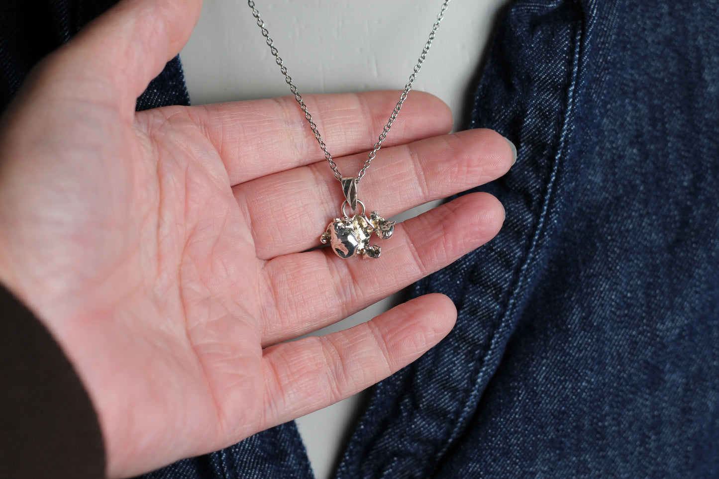 Close-up of a delicate 925 sterling silver pendant with a raw molten texture and a tiny 2mm blue sapphire gemstone set in the center.